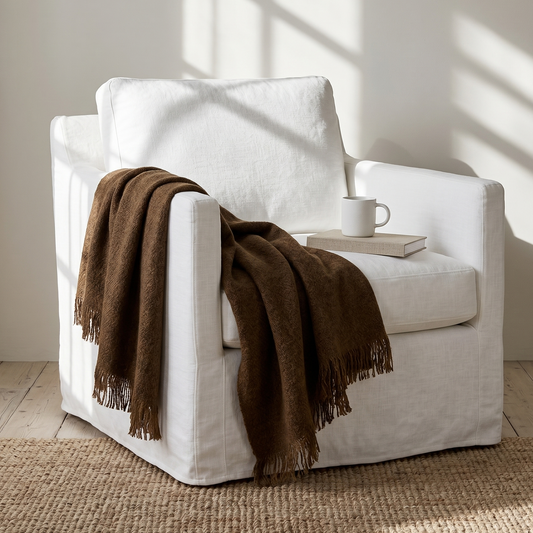 White armchair with a brown blanket and white mug on a wooden floor.