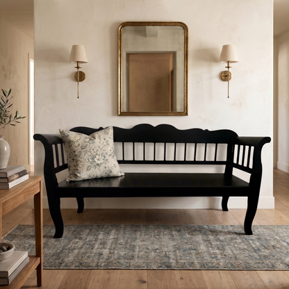 Black wooden bench in a living room with a mirror and lamp on the wall.