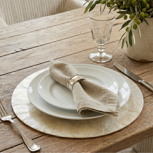 Dining table setting with plates, napkin, cutlery, and a vase of greenery.