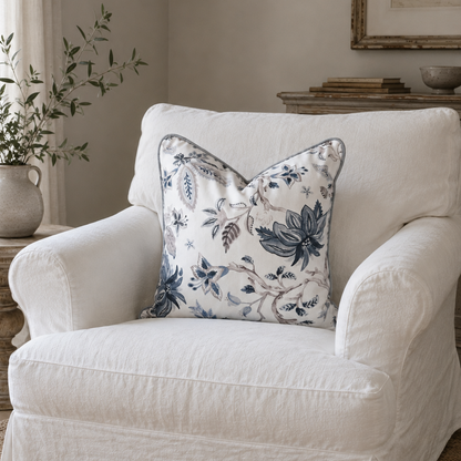 A white slipcovered armchair in a styled living room setting, featuring a decorative throw pillow with a blue and white floral pattern.