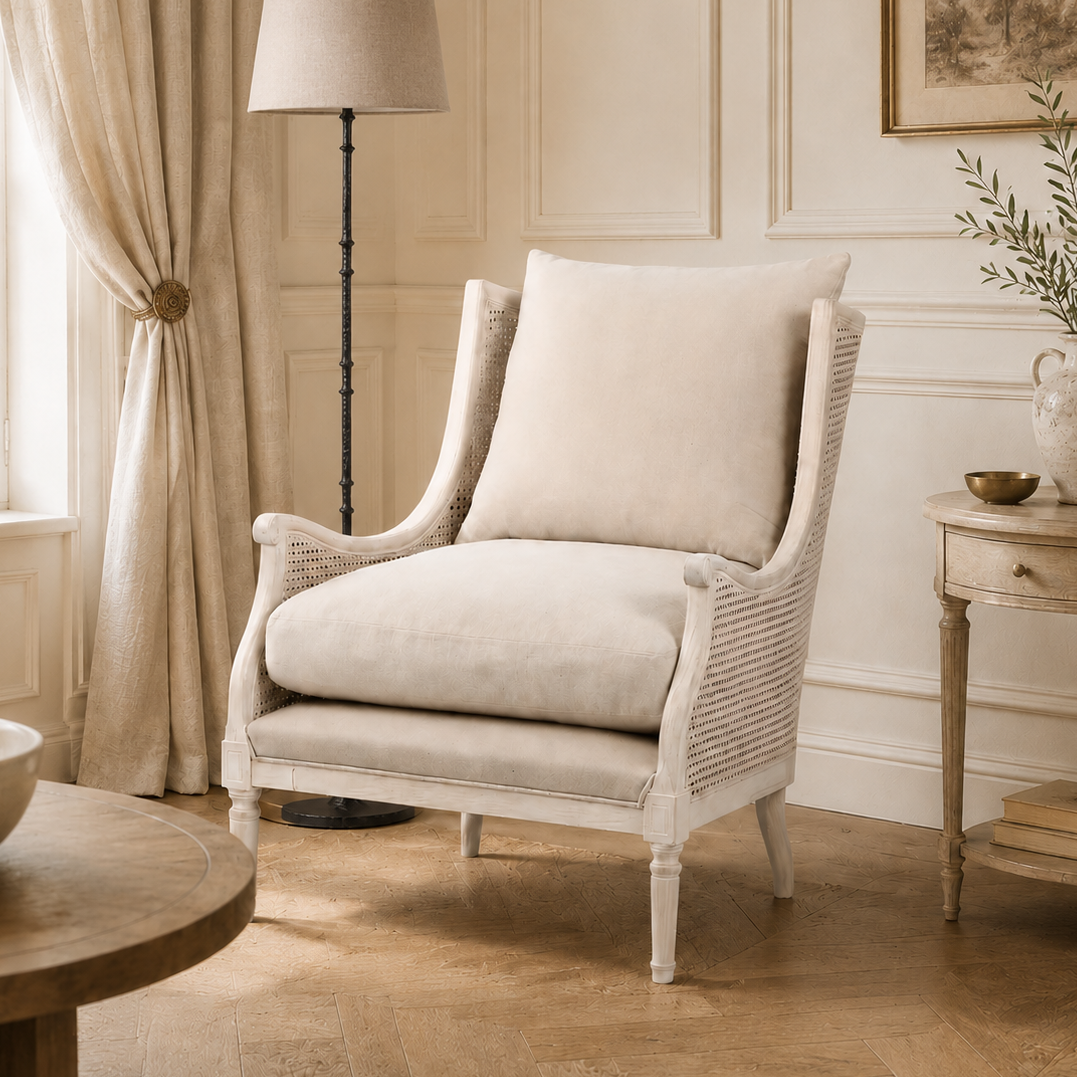 A classic white wicker armchair with plush cream cushions, styled in a bright, elegant room with beige walls, a floor lamp, and a side table.