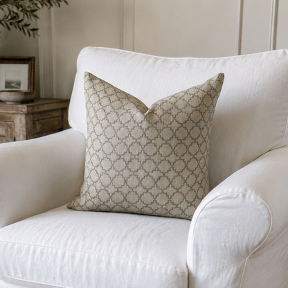A white slipcovered armchair in a cozy living room setting, styled with a beige patterned throw pillow.