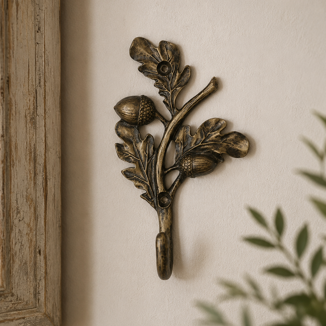 An ornate bronze-finished metal wall hook shaped like an acorn branch with leaves and acorns, mounted on a textured beige wall.