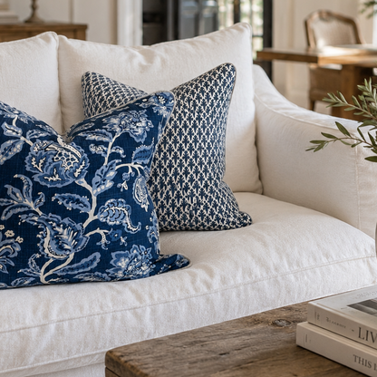 Two navy blue decorative throw pillows with intricate white and light blue patterns, styled on a white fabric sofa in a bright, modern living room.