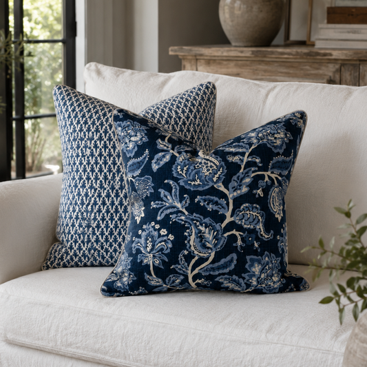 A white slipcovered sofa in a styled living room setting, featuring two navy blue decorative throw pillows with intricate floral and geometric patterns.