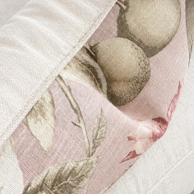 A close-up of a decorative throw pillow with a botanical pattern in soft pink, beige, and muted green, resting on a light beige upholstered armchair.