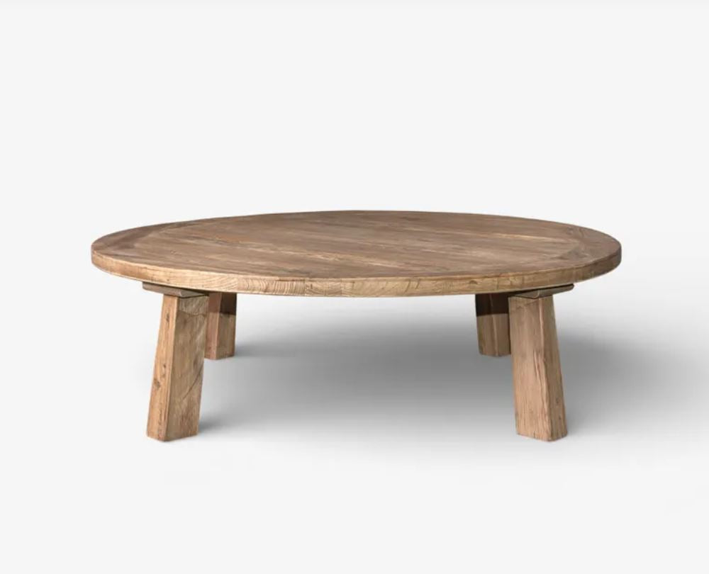 A round wooden low coffee table with chunky block legs, shown on a light gray background.