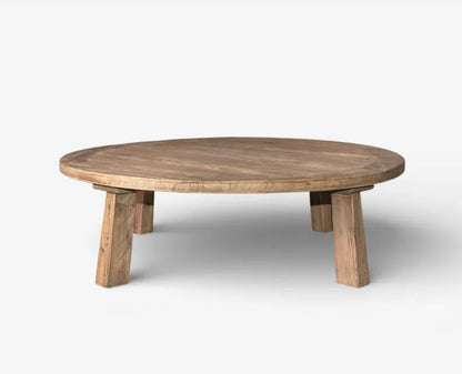 A round wooden low coffee table with chunky block legs, shown on a light gray background.