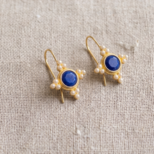 Gold earrings with blue stones on a beige fabric background