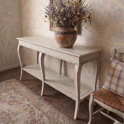 Vintage-style console table with a vase of flowers and mirror in a room with floral wallpaper.