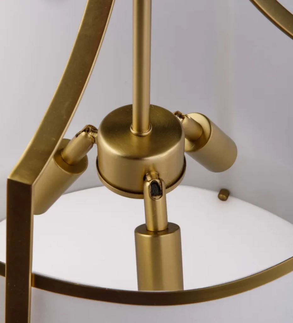 Close-up of a modern pendant light fixture with a brushed brass/gold metal frame and adjustable spotlight arms, set against a white shade.