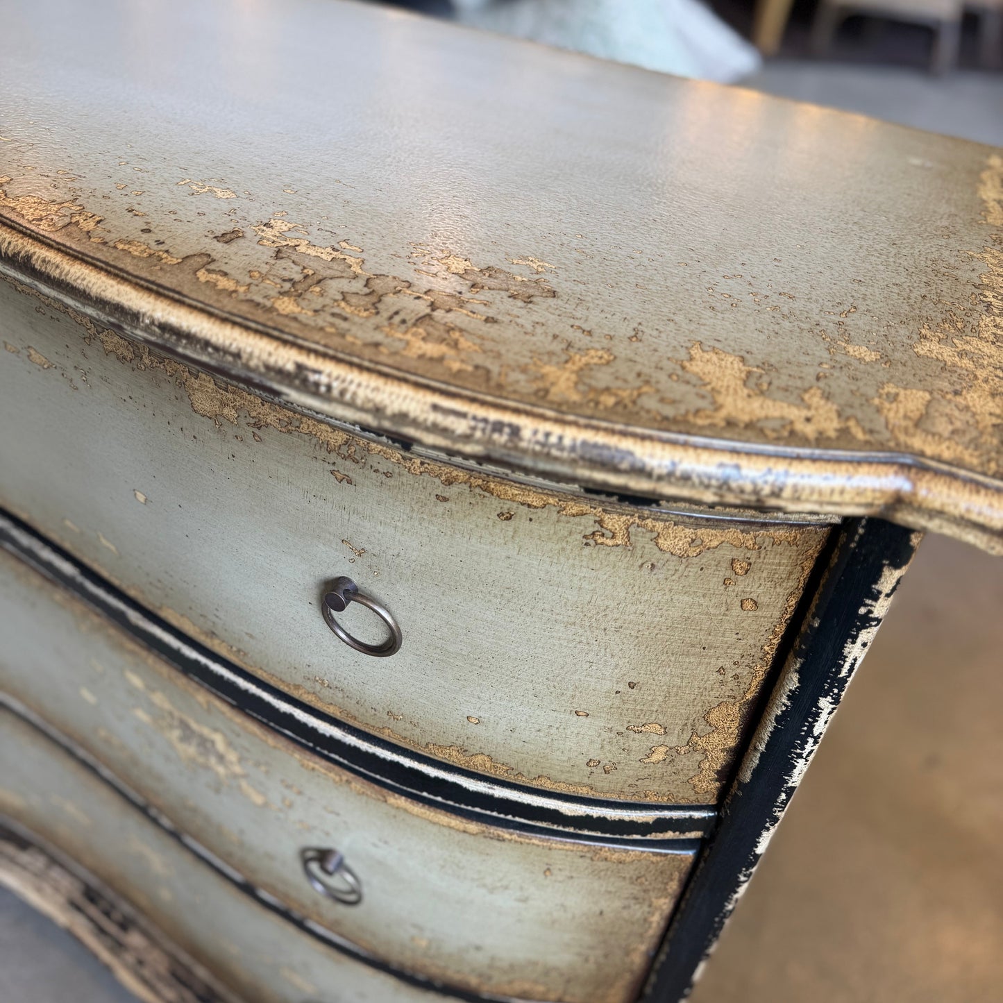 Decorative chest of drawers with gold leaf detailing in a blurred indoor setting