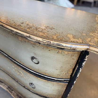 Decorative chest of drawers with gold leaf detailing in a blurred indoor setting