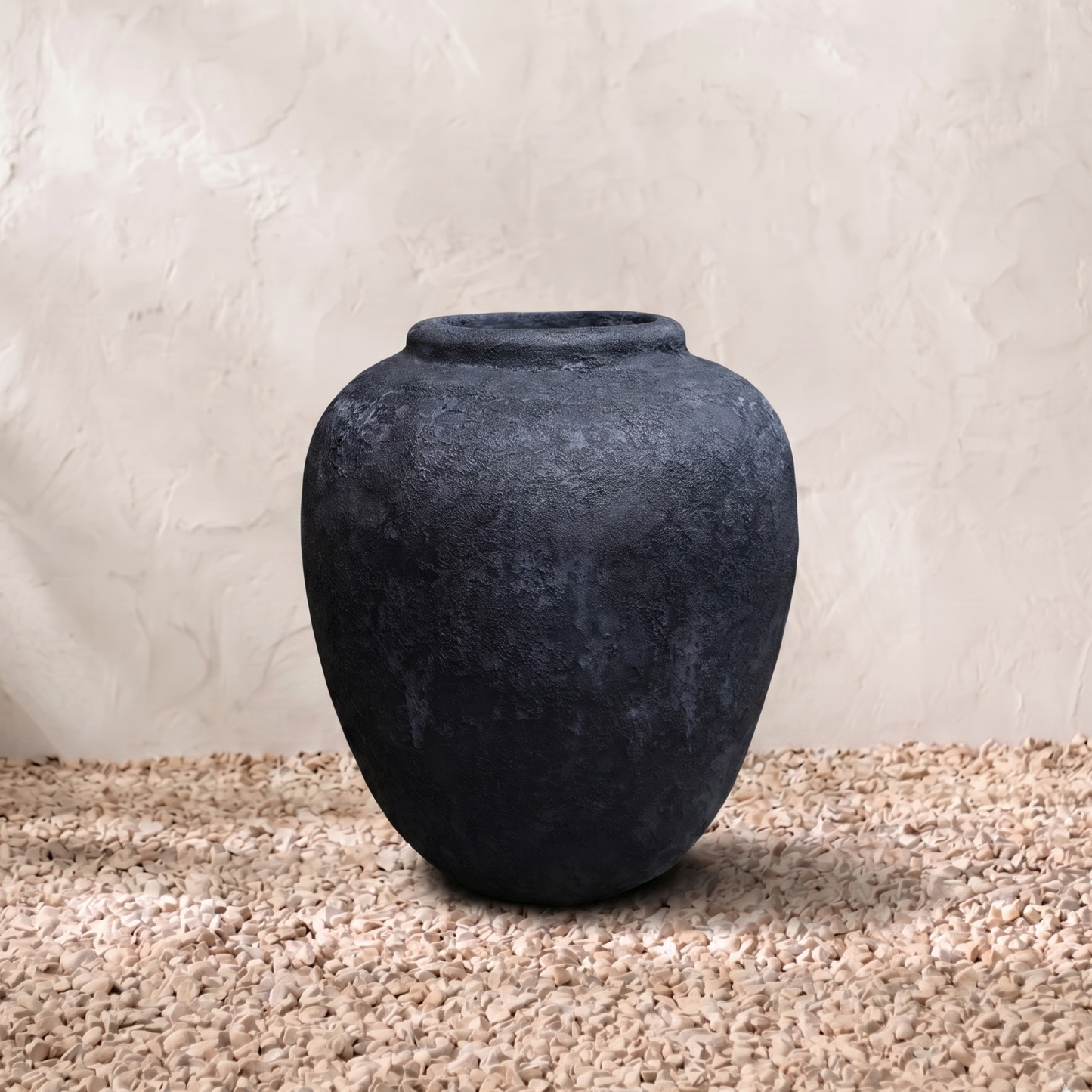 Dark gray textured vase on a beige surface with a light beige background
