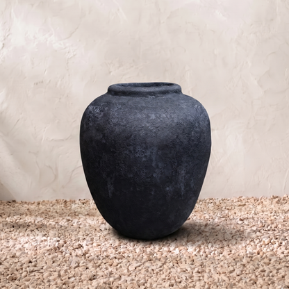 Dark gray textured vase on a beige surface with a light beige background