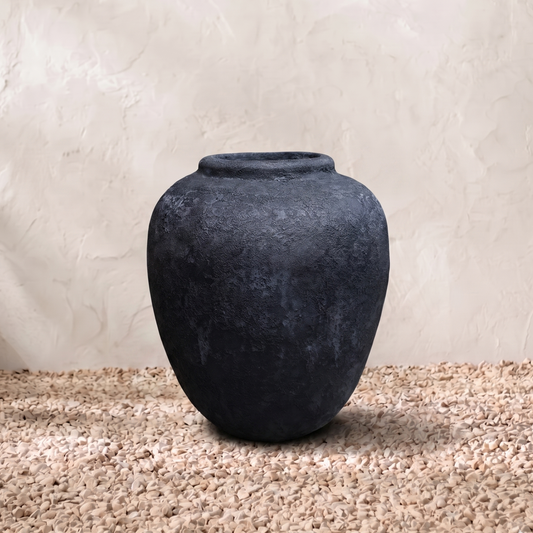 Dark gray textured vase on a beige surface with a light beige background