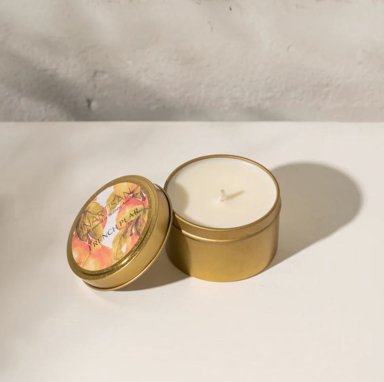 Gold tin candle with a lit candle inside on a light background