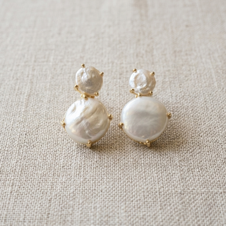 Pair of pearl earrings on a textured beige surface