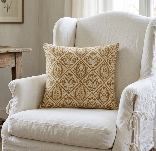 White armchair with a patterned pillow in a room with a wooden table and framed picture.