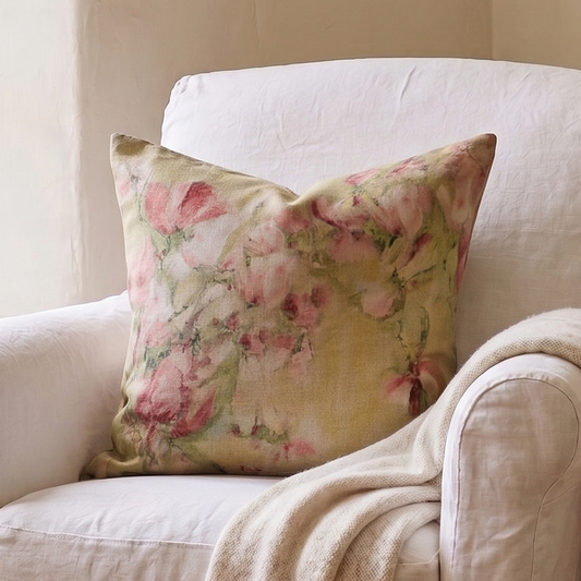 White armchair with floral pillow and blanket in a room with a window and small table.