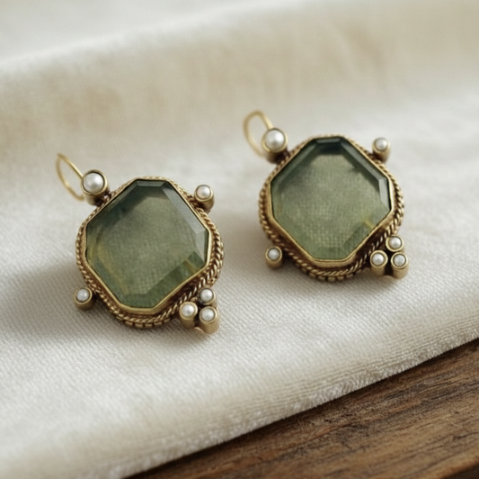Pair of earrings with green gemstones and gold frames on a white fabric background