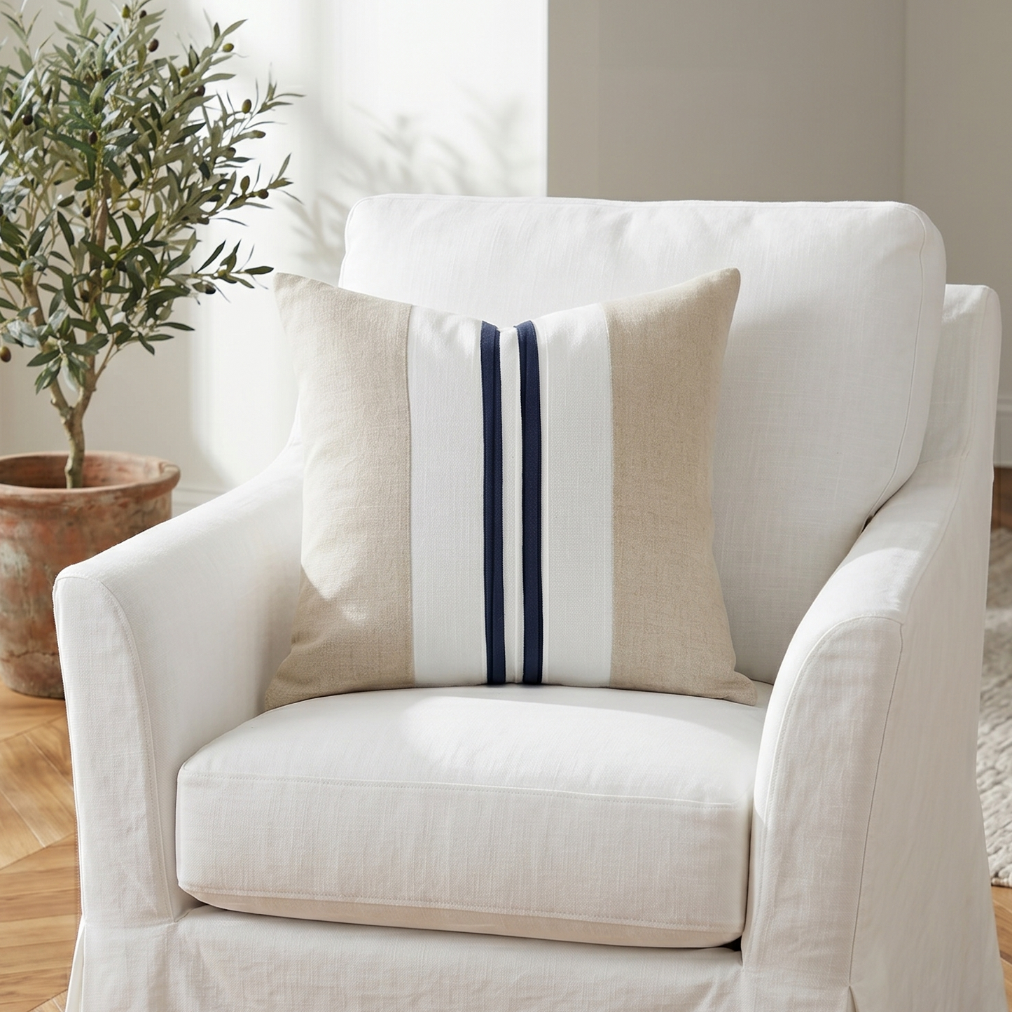 White armchair with a decorative pillow on a wooden floor, featuring a plant in the background.