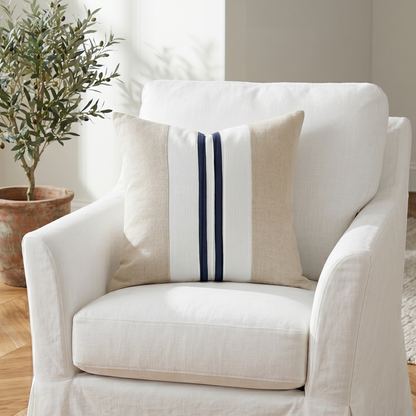White armchair with a decorative pillow on a wooden floor, featuring a plant in the background.