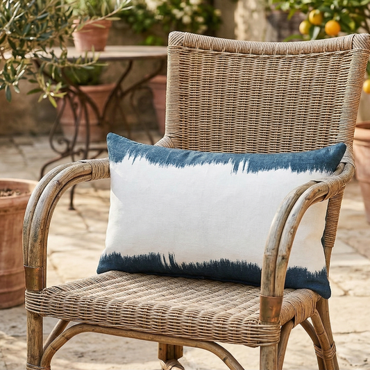 Wicker chair with a blue and white pillow in an outdoor setting with potted plants.