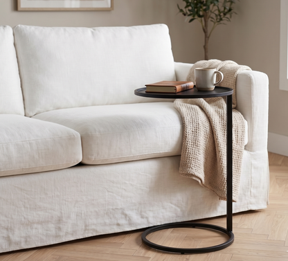 White sofa with a black side table holding a mug and book, in a cozy living room setting.