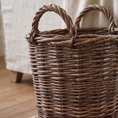 Woven basket on a wooden floor with a textured rug and light-colored fabric in the background