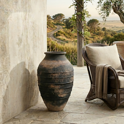 Wicker chair with a blanket next to a large urn on a stone patio with a scenic view.