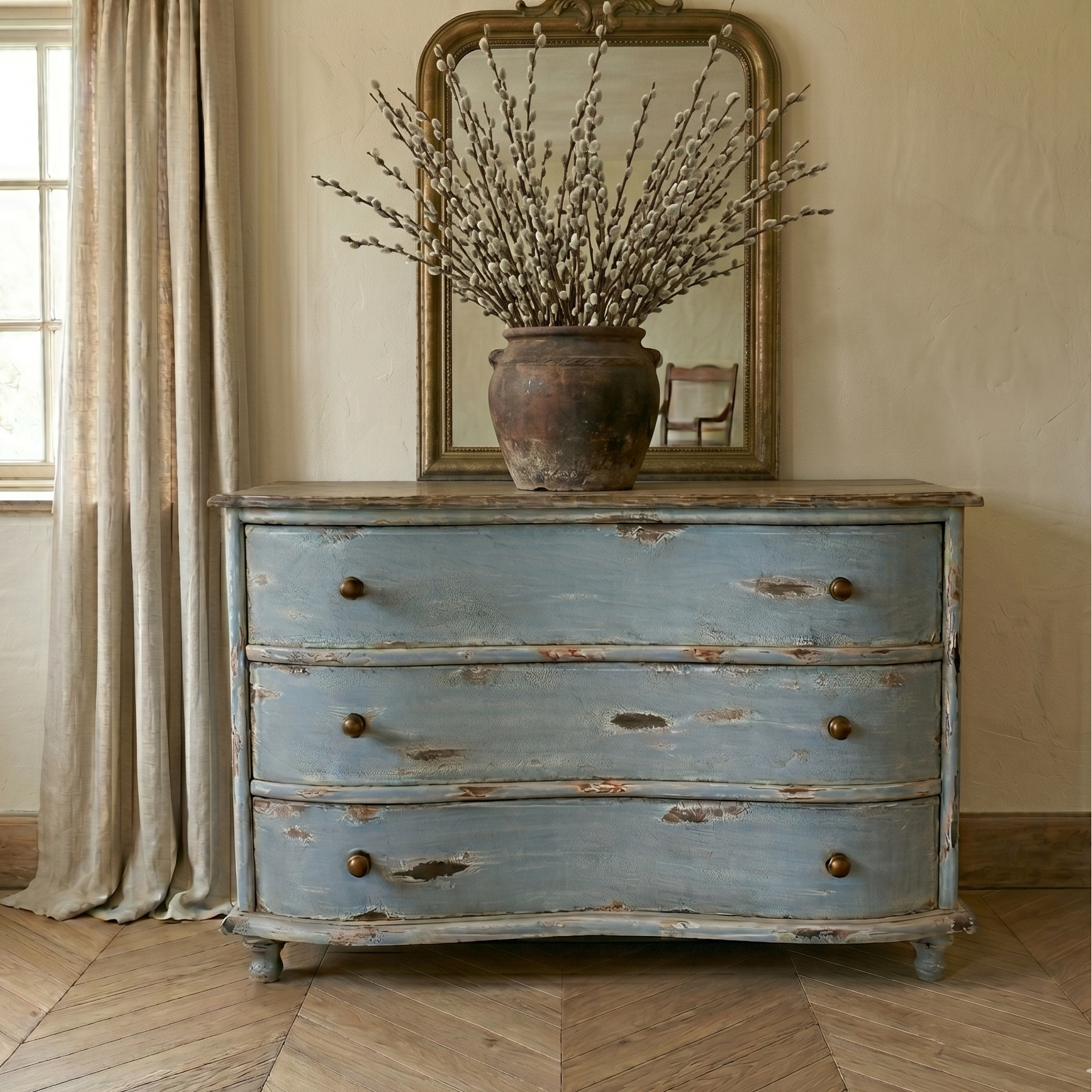 Vintage blue dresser with a mirror and decorative plant in a room with wooden floor and window.