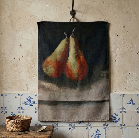 Teatowel with pear design hanging on a wall next to a wooden stool with a basket and spoon.