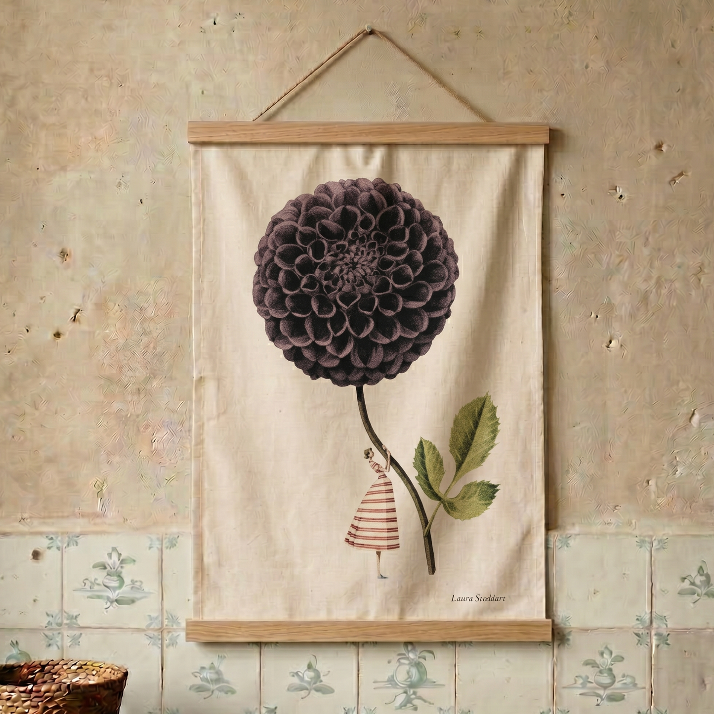 Decorative tea towel with a large purple flower and a small figure on a beige background, hanging on a textured wall.