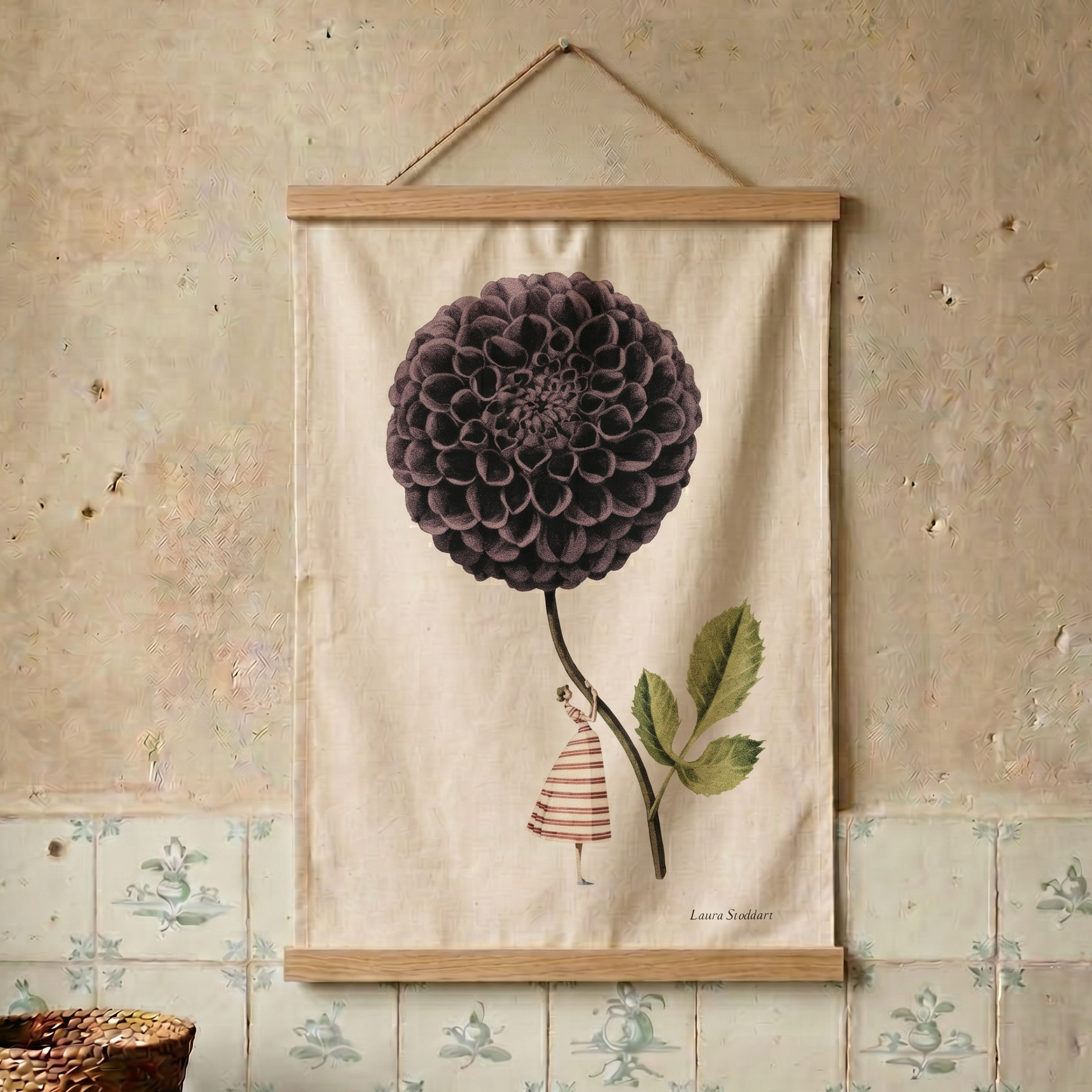 Decorative tea towel with a large purple flower and a small figure on a beige background, hanging on a textured wall.
