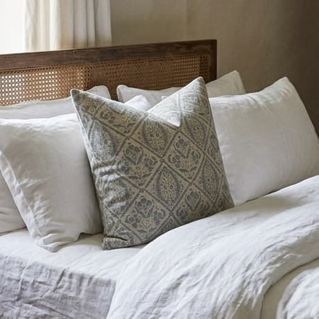 Bed with white bedding and a decorative pillow against a neutral wall.