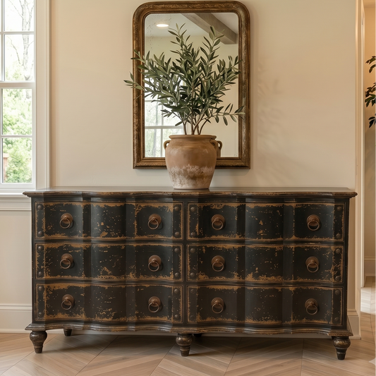 Vintage-style dresser with a mirror and potted plant in a room with wooden flooring.