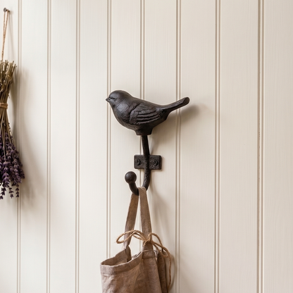 Wall hook with a bird design, lavender bundle, and bag against a wooden surface and paneled wall.