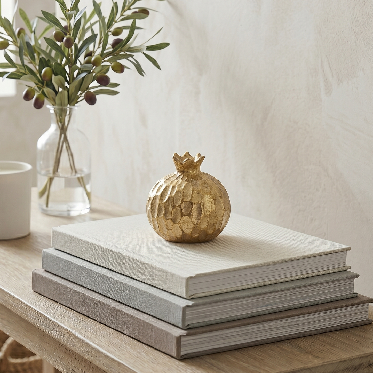 Stack of books on a wooden surface with a gold decorative item and a vase with greenery.