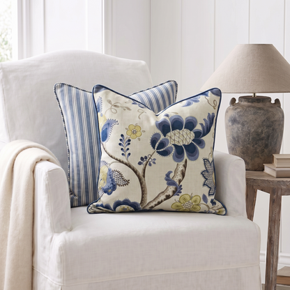 Decorative pillows on a white armchair with a lamp and vase in the background