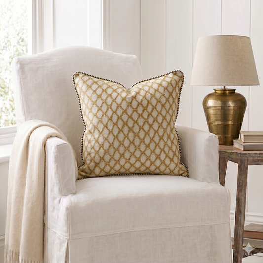 White armchair with a decorative pillow and gold lamp in a room with white walls.