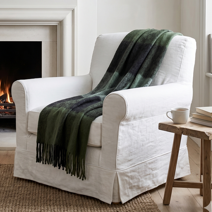White armchair with a green blanket in front of a fireplace in a cozy living room.