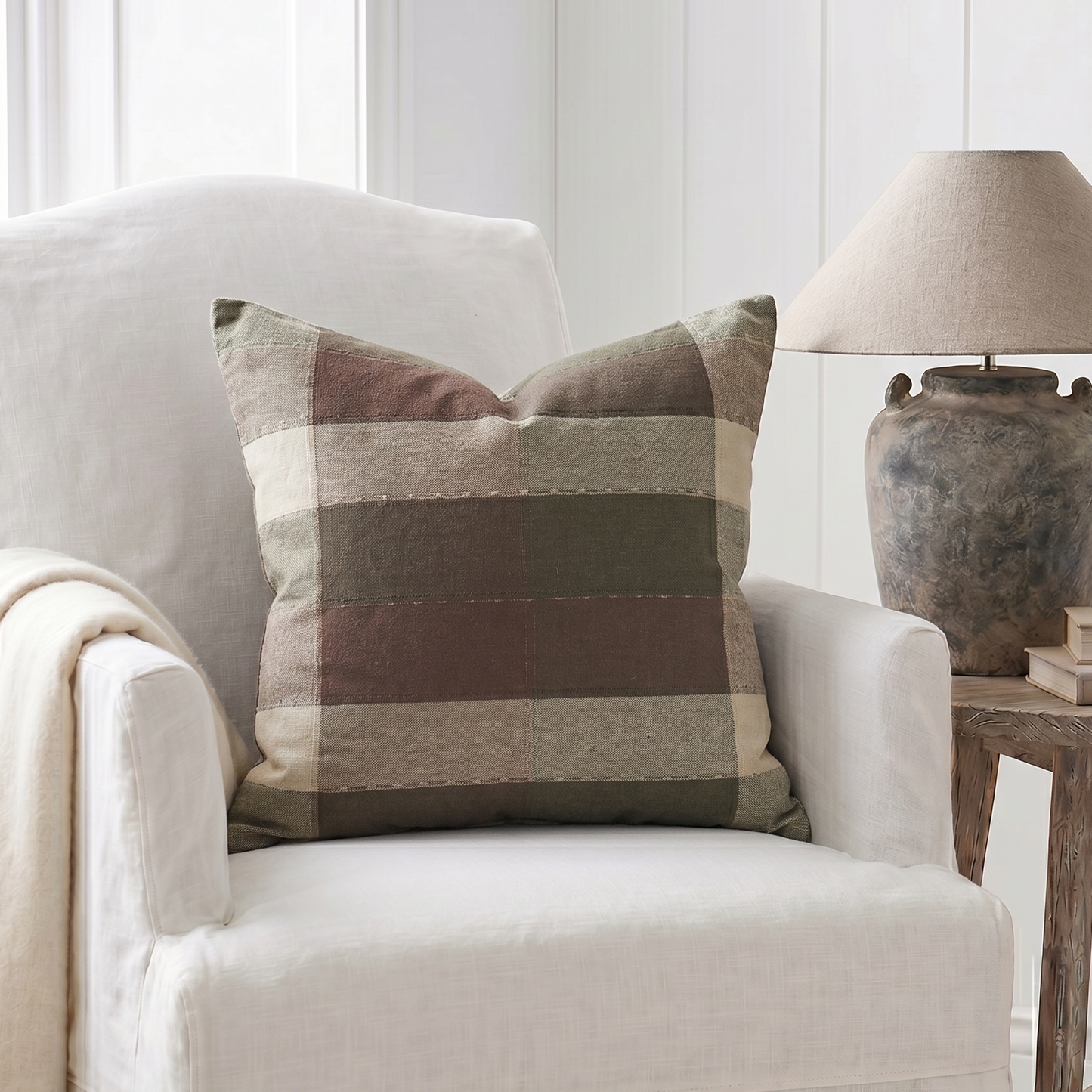 White armchair with a plaid pillow and a lamp in a room with white walls.