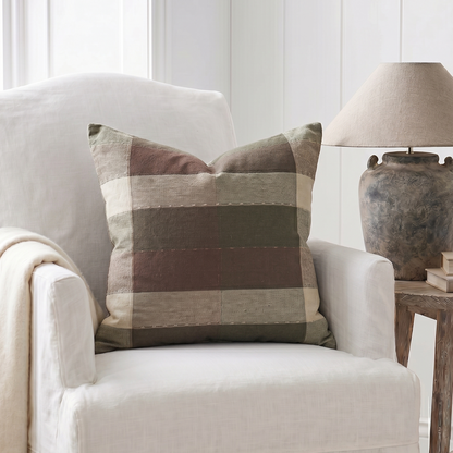 White armchair with a plaid pillow and a lamp in a room with white walls.