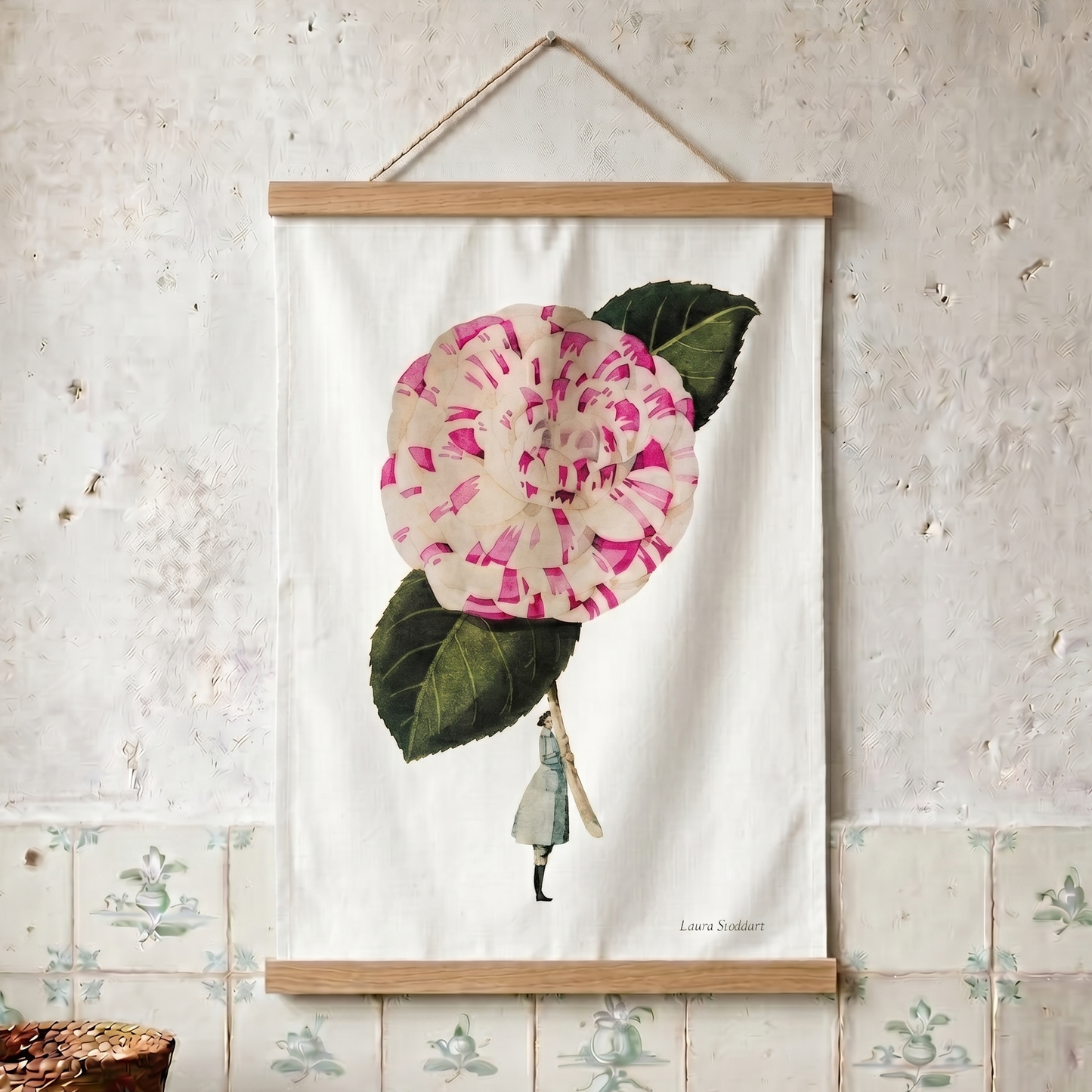 Tea towel with a pink flower and green leaves hanging on a textured wall.