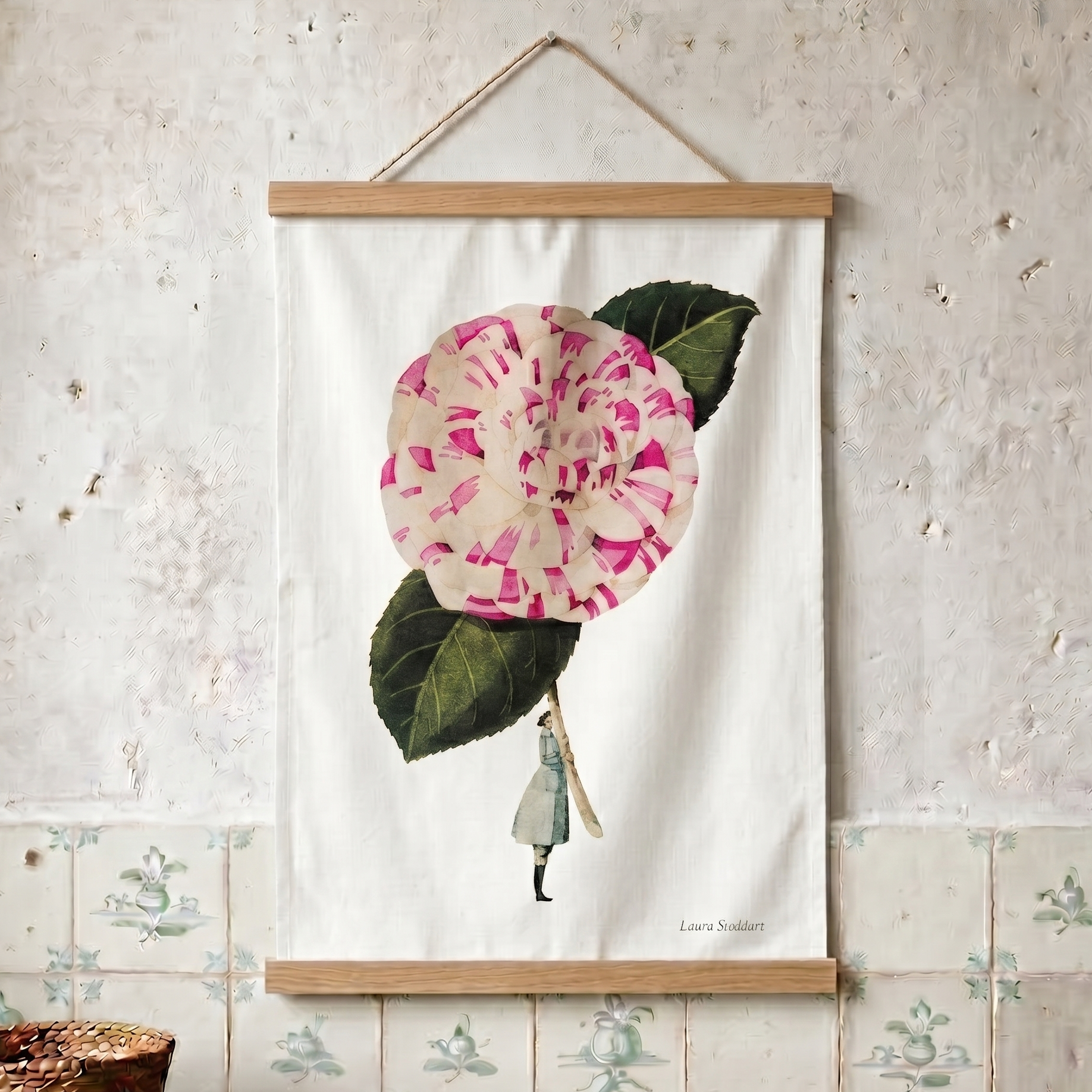 Tea towel with a pink flower and green leaves hanging on a textured wall.
