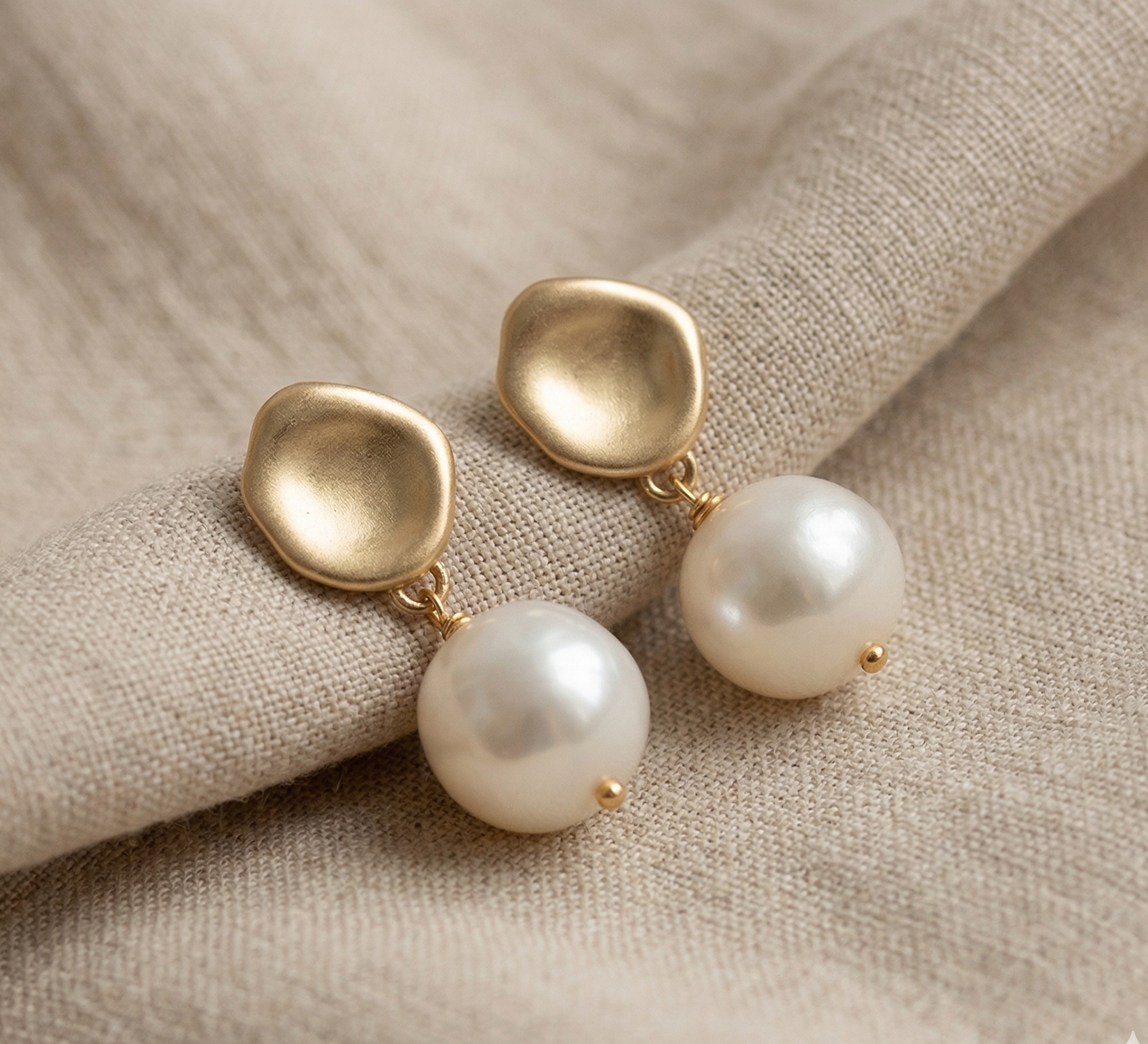 Gold earrings with pearls on a beige fabric background