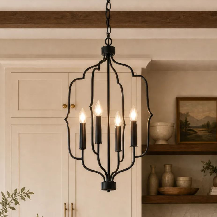 A black metal five-light chandelier with a decorative open frame hangs in a warm, rustic kitchen setting with cream cabinets and wooden beams.