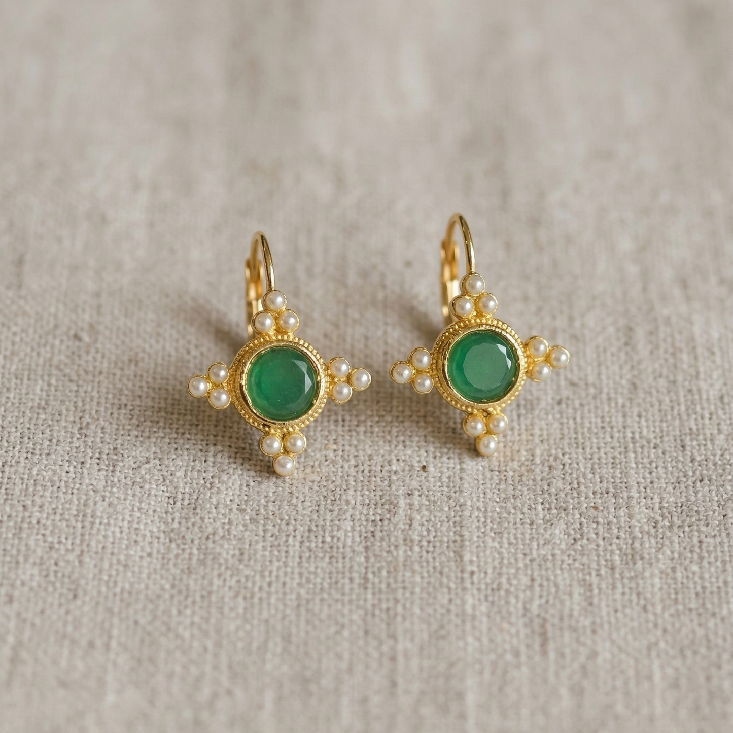 Pair of gold earrings with green gemstones on a textured beige background