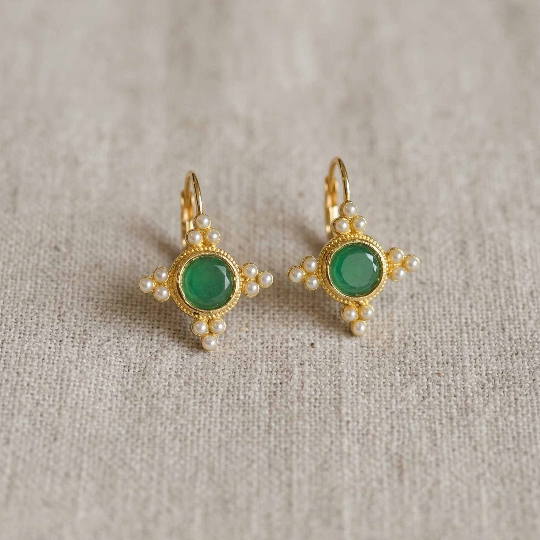 Pair of gold earrings with green gemstones on a textured beige background